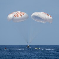 Une capsule amerrit dans l'océan, ralentie par quatre parachutes.