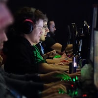 Plusieurs joueurs enlignés sur une longue table, regardant leur écran et les mains sur le clavier, jouant à un jeu vidéo lors d'une compétition.