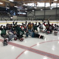 Une vingtaine de joueurs de para-hockey sourient au centre de la glace.