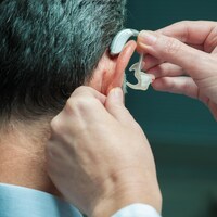 Un médecin insère une prothèse auditive dans l'oreille d'un homme.