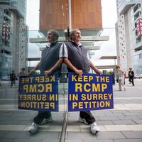 Un homme tient une pancarte qui appelle à signer une pétition en faveur du maintien de la GRC à Surrey.