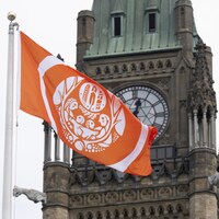 Un drapeau orange cohabite avec la tour de l'édifice du Parlement à Ottawa.