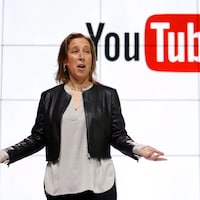 Susan Wojcicki est debout devant un écran sur lequel est affiché le logo de YouTube. 