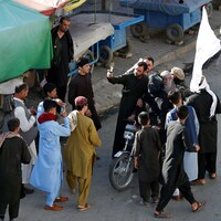 Plusieurs résidents de Kaboul entourent trois talibans assis sur une motocyclette. Deux d'entre eux prennent un égoportrait avec eux pendant qu'un autre photographie la scène.