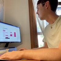Un homme est assis chez lui devant son écran d'ordinateur. Il regarde son horaire pour la semaine à venir.