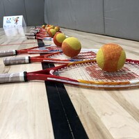 Des raquettes de tennis avec des balles alignées par terre dans un gymnase.