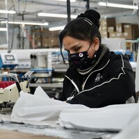 Une couturière avec un masque qui coud une blouse de protection dans l'usine.