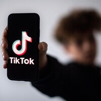 Un jeune homme flouté tient un téléphone intelligent affichant le logo de TikTok. 
