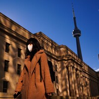 Une femme masquée marche au centre-ville de Toronto, près de la tour du CN.