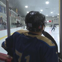 Un joueur de hockey regarde le déroulement du jeu debout derrière la bande. 