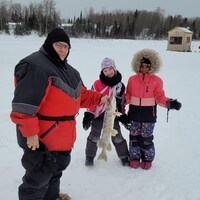 Une personne tient un poisson sur un lac en hiver avec deux enfants derrière
