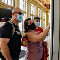 Trois personnes masquées achètent des billets de transport à un distributeur.