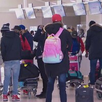 Des dizaines de personnes attendent devant les bureaux d'enregistrement de l’Aéroport Pearson de Toronto avec leurs valises en main et un masque sur le visage.