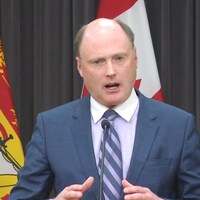 Trevor Holder entre deux drapeaux du Nouveau-Brunswick.