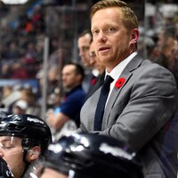 Trevor Letowski est debout derrière des joueurs de hockey sur le côté de la patinoire.