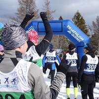 Plusieurs athlètes se positionnent à la ligne de départ d'un triathlon d'hiver. Ils portent des dossards pour distinguer les diverses catégories. 