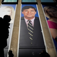 Des personnes passent devant les publicités des animateurs de Fox News, dont Tucker Carlson, apposées à l'édifice de la News Corporation, à New York.