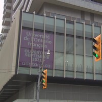 Une affiche dans la fenêtre d'un immeuble à une intersection annonce l'ouverture de l'Université.