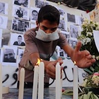 Un jeune homme allume des bougies devant des photos en noir et blanc de victimes des explosions.