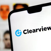 Un écran montrant le logo de Clearview AI avec des visages embrouillés à l'arrière.