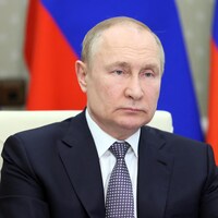 Vladimir Poutine assis devant des drapeaux.