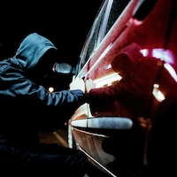 Un voleur de voiture en action tard dans la nuit, portant des vêtements noirs.