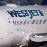 Un gros plan d'un avion du transporteur WestJet, vu de l'extérieur. On voit un pilote assis dans la cabine.