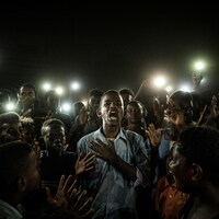 Un jeune homme, illuminé par des téléphones cellulaires, récite un poème entouré d'une foule au Soudan.
