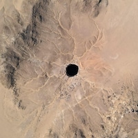 Vue aérienne éloignée du puits de Barhout : un trou noir au milieu du désert.