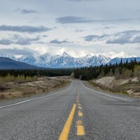 Une route allant vers des montagnes enneigées au Yukon.
