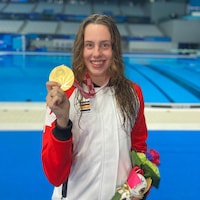 Aurélie Rivard montre fièrement sa médaille et tient son bouquet devant la piscine du Centre aquatique de Tokyo. 