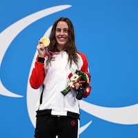 Aurélie Rivard pose fièrement, médaille d'or au cou, sur la première marche du podium paralympique à Tokyo. 