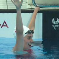 Aurélie Rivard lève les bras en l'air et sourit dans l'eau en se tenant sur le bord de la piscine.