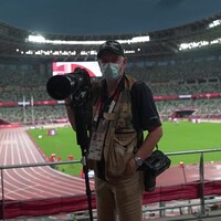 Bernard Brault tient un appareil photo et un trépied dans le stade olympique de Tokyo.