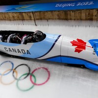 Quatre athlètes canadiens accroupis dans leur bobsleigh dévalent la piste.