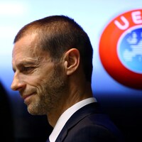 Un homme de profil sourit timidement devant un logo de l'UEFA.