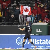 Le joueur Alistair Johnston porte le drapeau canadien devant des partisans à Edmonton.
