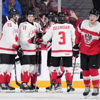 Des hockeyeurs canadiens célèbrent un but tout près d'un rival autrichien.
