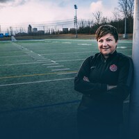 Carol Anne Chénard est appuyée sur un but de soccer et sourit.