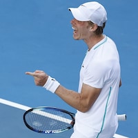 Un joueur est heureux sur un court de tennis, et pointe l'index de sa main gauche.