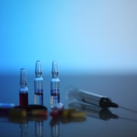 Sur une table, quatre ampoules avec du liquide à l'intérieur, une seringue et des pilules.