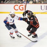Deux joueuses de hockey canadienne et américaine sont sur le glace face à face. 