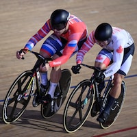 Deux cyclistes sur piste s'affrontent dans un sprint. 