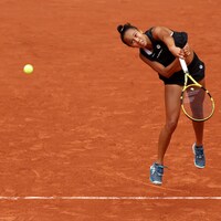Une joueuse de tennis vêtue de noir regarde la balle qu'elle vient de frapper en service au tournoi de Roland-Garros. 