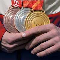 Un athlète tient trois médailles entre ses mains, une en or, une en argent et une en bronze.