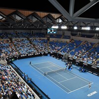 Vue générale d'un court intérieur de tennis pendant un match, avec quelques personnes dans les gradins