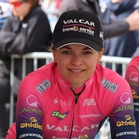 La cycliste, vêtue du maillot et de la casquette de son équipe, pose pour une photo. 