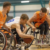 Des joueurs de la Finlande, en bleu, et des Pays-Bas, en orange, luttent pour le ballon dans un match de basketball en fauteuil. 