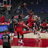 Un joueur de basketball tente d'inscrire un panier malgré la présence d'adversaires autour de lui.