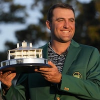 Le golfeur, vêtu d'un veston vert, présente son trophée.
